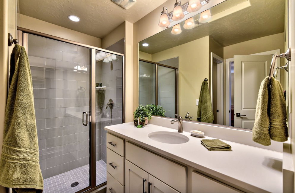 Spacious bathroom featuring a glass-enclosed shower with subway tile surround, a large vanity with an integrated sink, and a wall-mounted mirror with overhead lighting