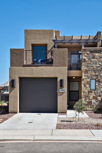Stucco exterior with stone accent facade, featuring a dark tone garage door, an upper balcony with metal railing, and a second-story patio with pergola