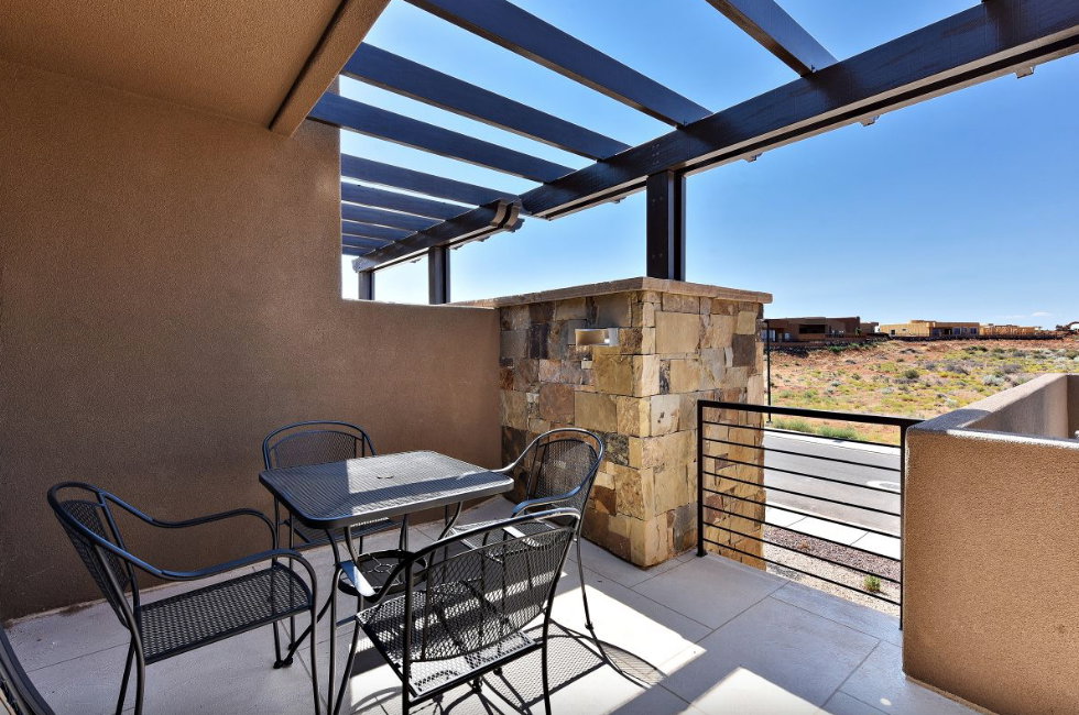 Outdoor patio featuring an open pergola, stucco walls, stone accent pillar, black metal railing, and concrete flooring