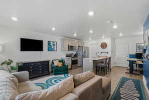 Open-concept living space featuring wood-finish flooring, recessed lighting, and a kitchen island with seating