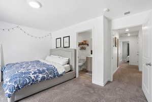 Bedroom with plush carpeting, recessed ceiling lighting, and a private en-suite bathroom featuring wood-finish flooring and a vanity with a light-colored countertop