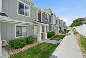 Exterior featuring light gray vertical siding, white trim, a stone accent column, a covered entry, and a clear concrete walkway