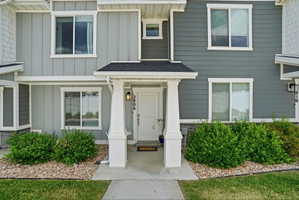 Entryway featuring a covered porch with white columns, a dark gray shingled roof, and a white front door with a brass-finish exterior light fixture