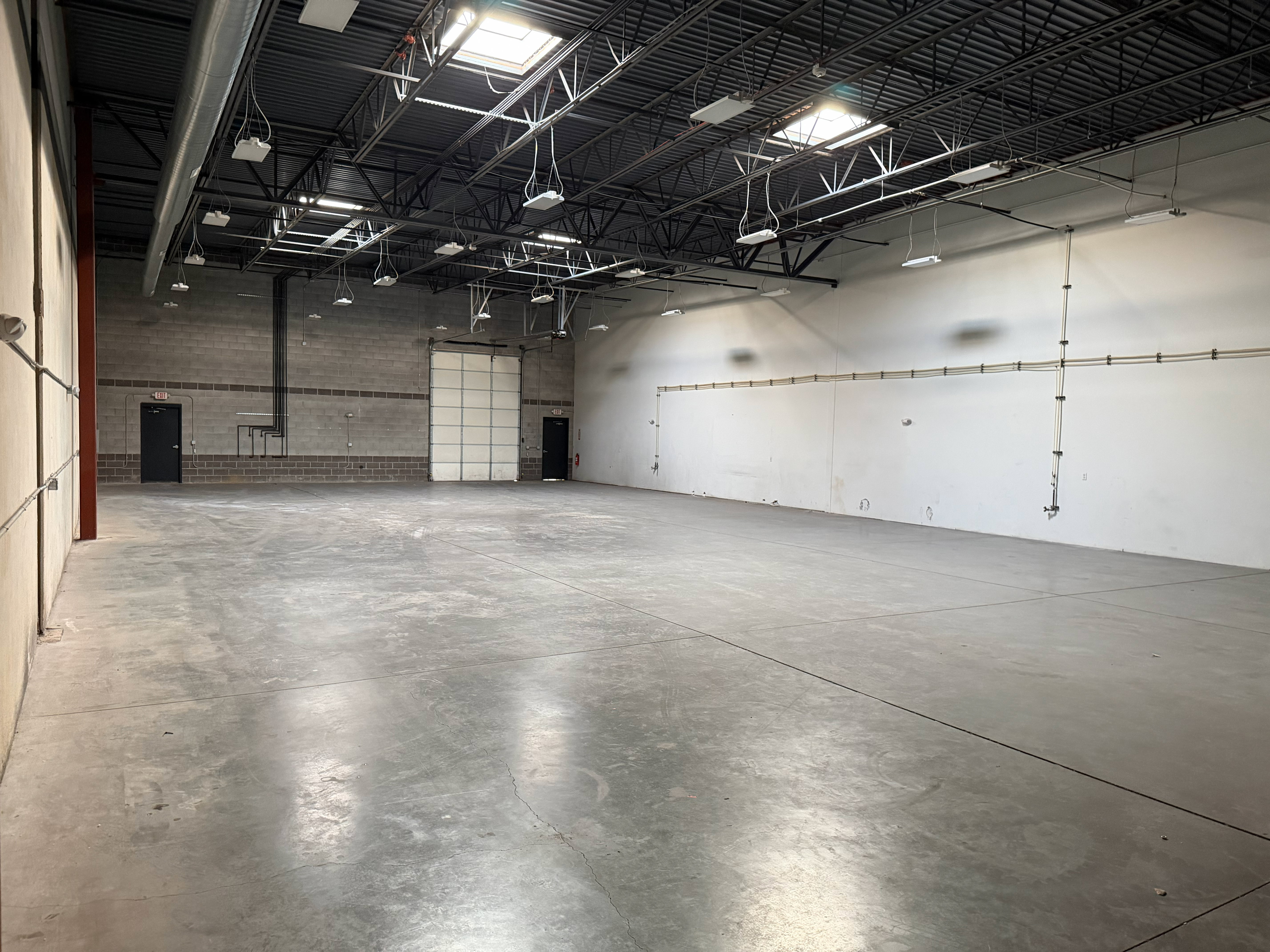 Spacious commercial warehouse featuring an overhead garage door, two entry doors, and durable concrete flooring