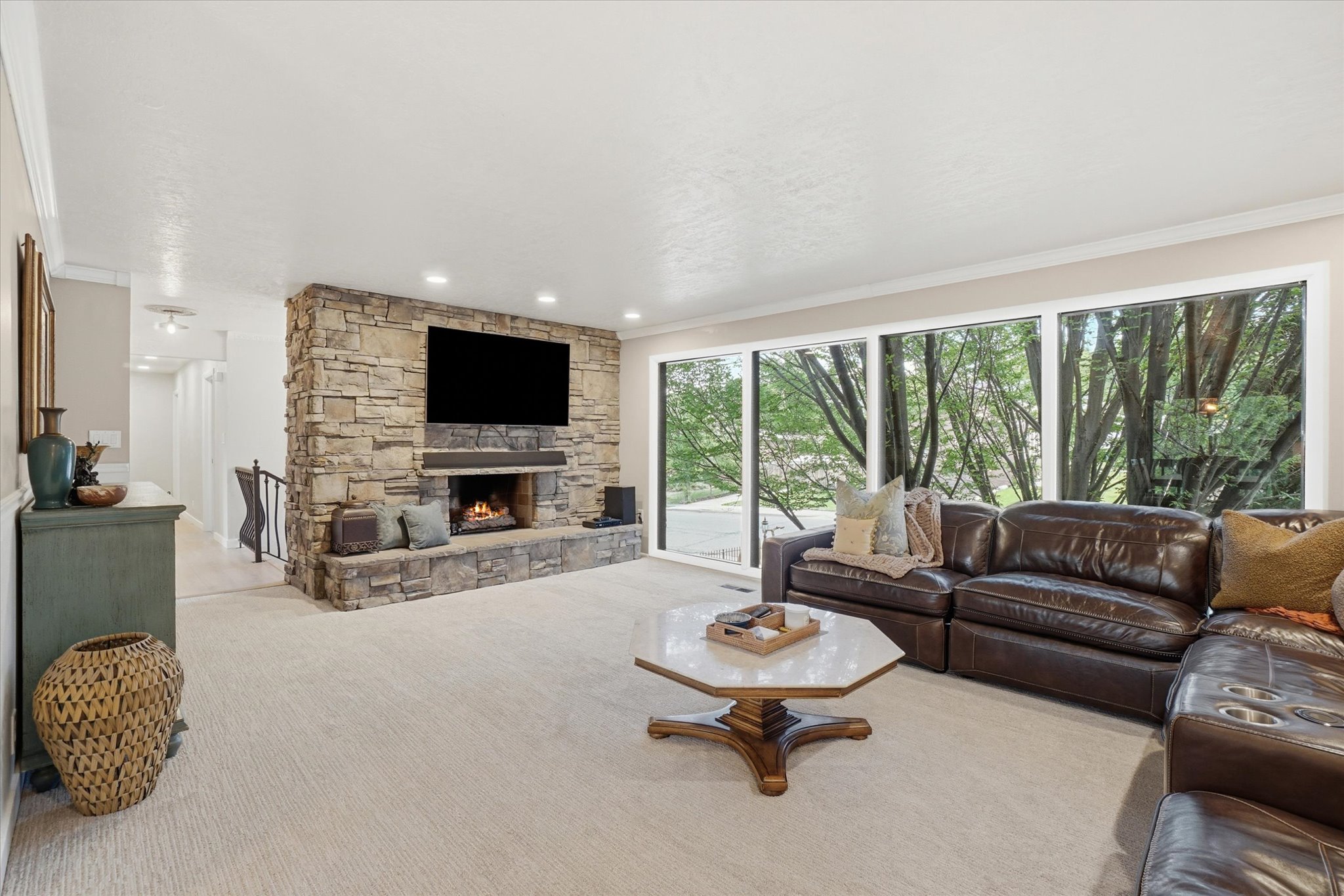 Spacious living area featuring a stone-clad fireplace and hearth, recessed lighting, and expansive windows