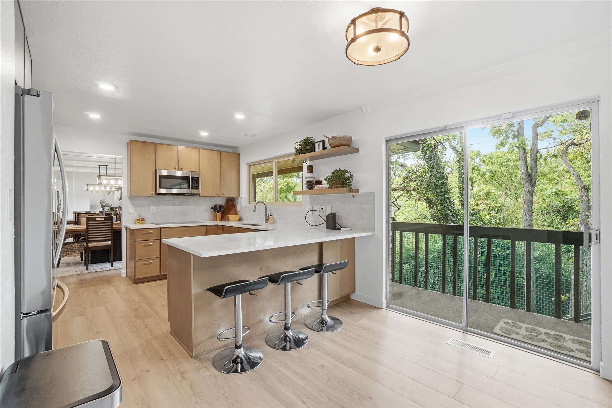 Open-concept kitchen featuring light wood-finish cabinetry, a white subway tile backsplash, stainless steel appliances, and a central island with a white countertop and seating