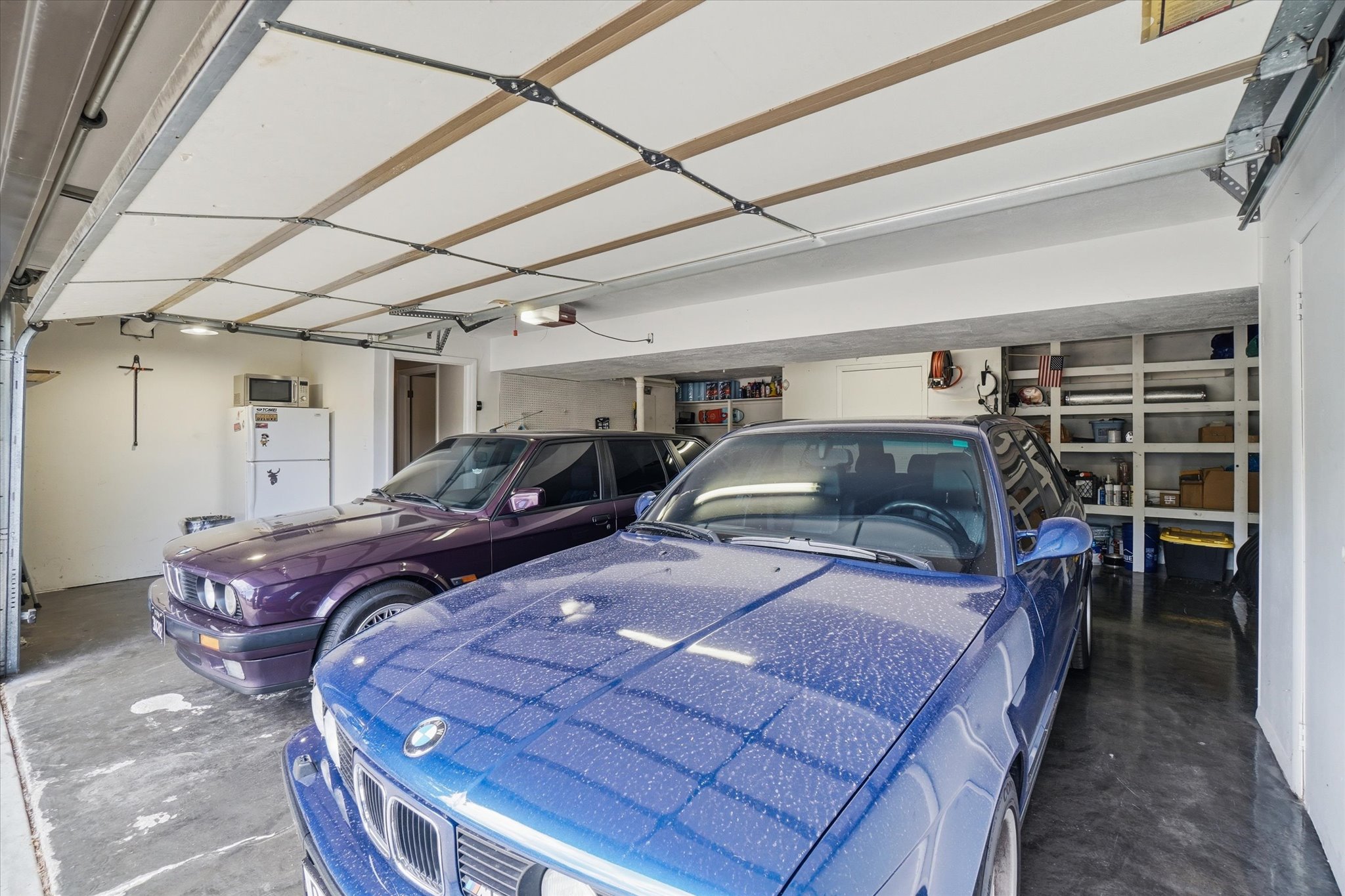 Attached two-car garage featuring a concrete floor, built-in shelving, and white interior walls