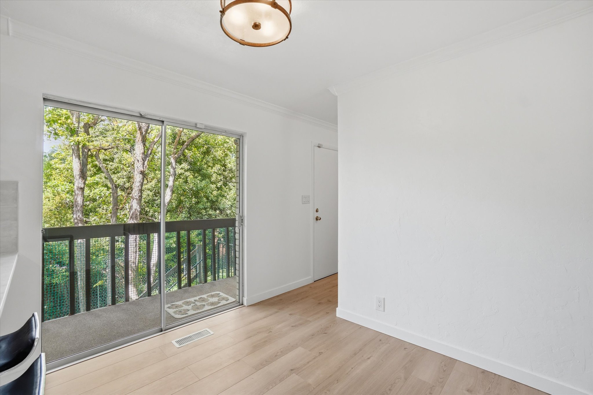 Sliding glass doors opening to a balcony with dark railings, surrounded by lush trees