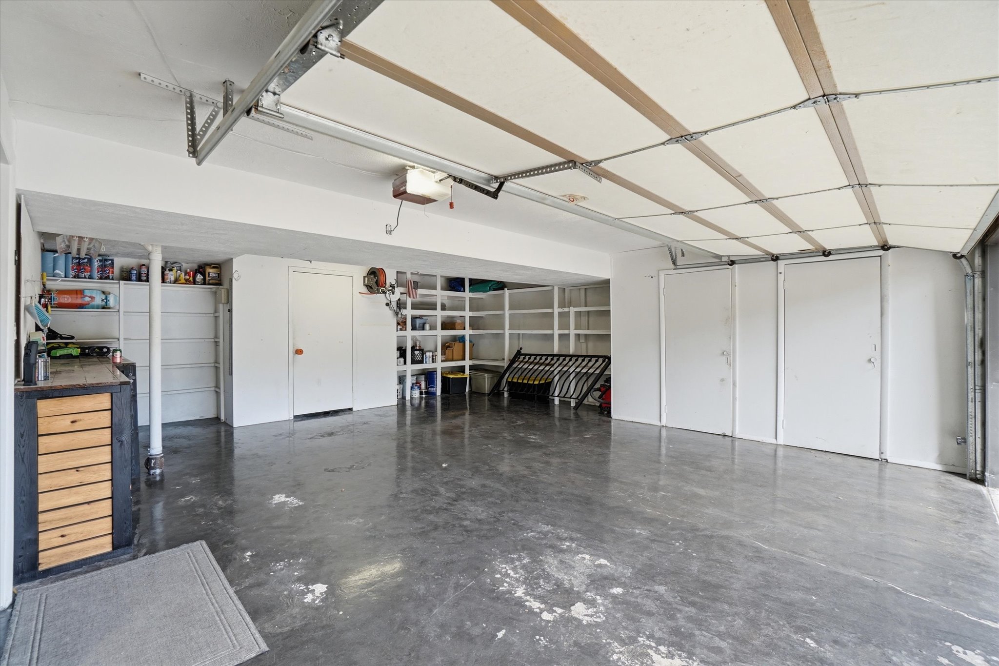 Spacious garage featuring a finished concrete floor, built-in shelving, two interior access doors, and an overhead garage door mechanism