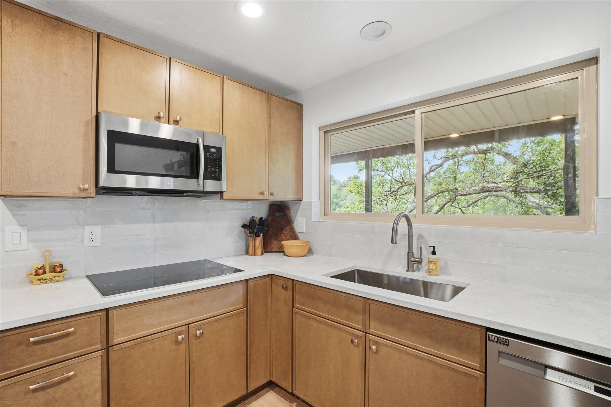 Modern kitchen featuring light wood cabinetry, white countertops, and a white tile backsplash