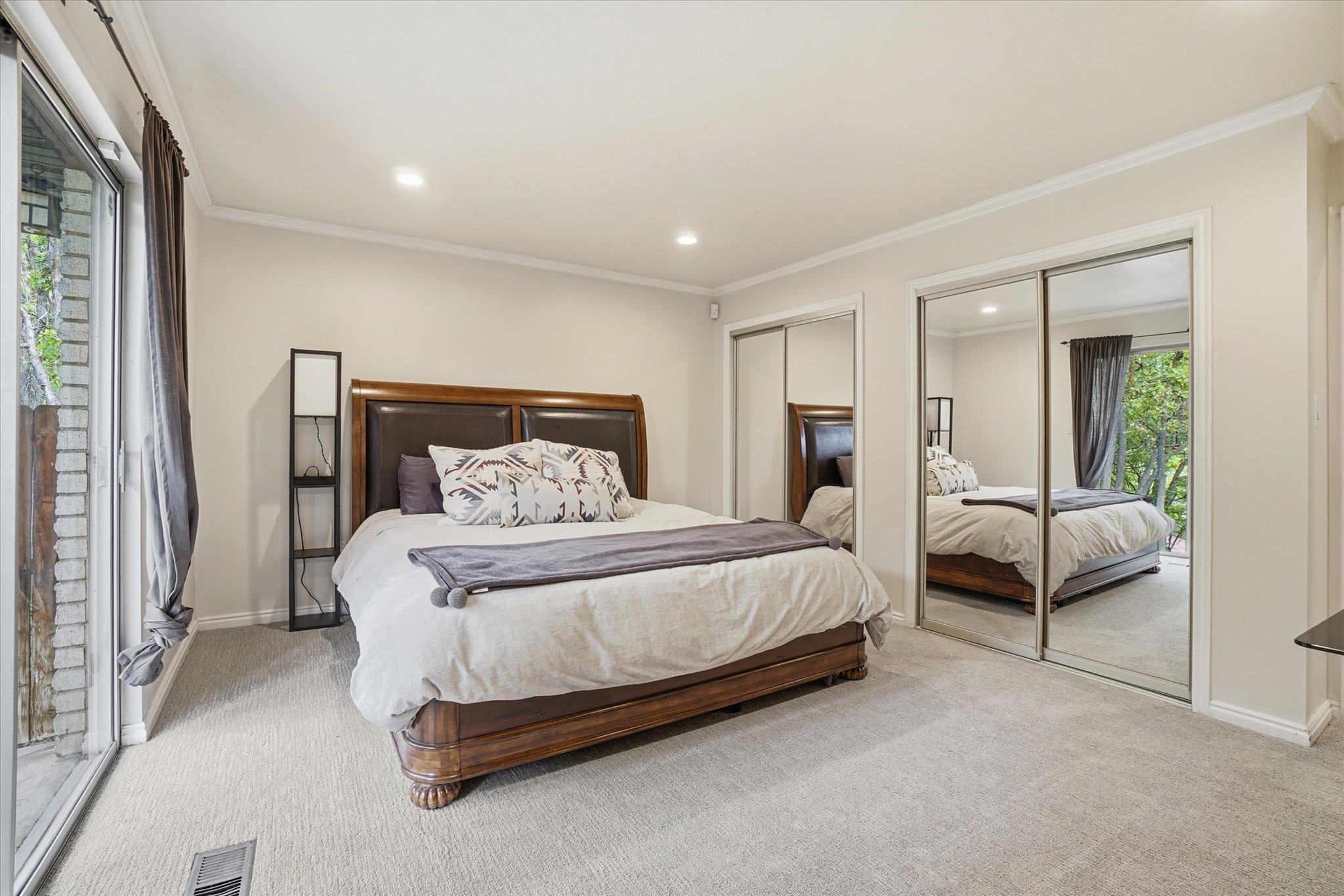 Carpeted room featuring a sliding glass door, recessed lighting, crown molding, and two mirrored closet doors