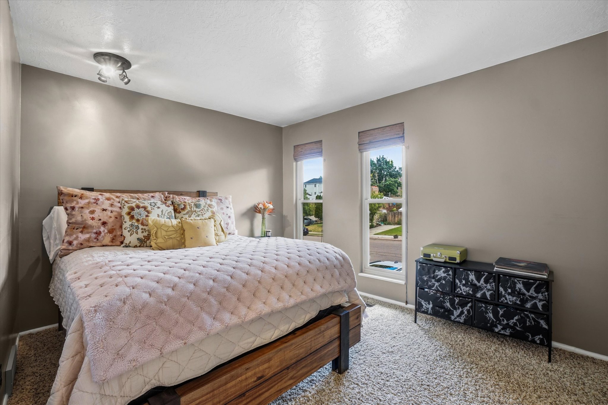 Bedroom featuring neutral wall paint, two tall windows with shades, and plush carpet flooring