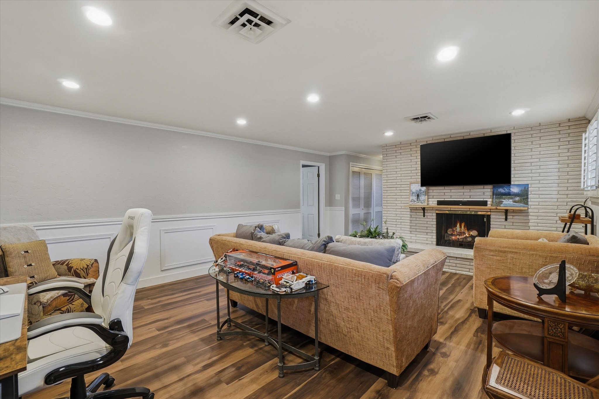 Living area featuring a white brick fireplace with a wood mantel, wood-finish flooring, recessed lighting, and white wainscoting