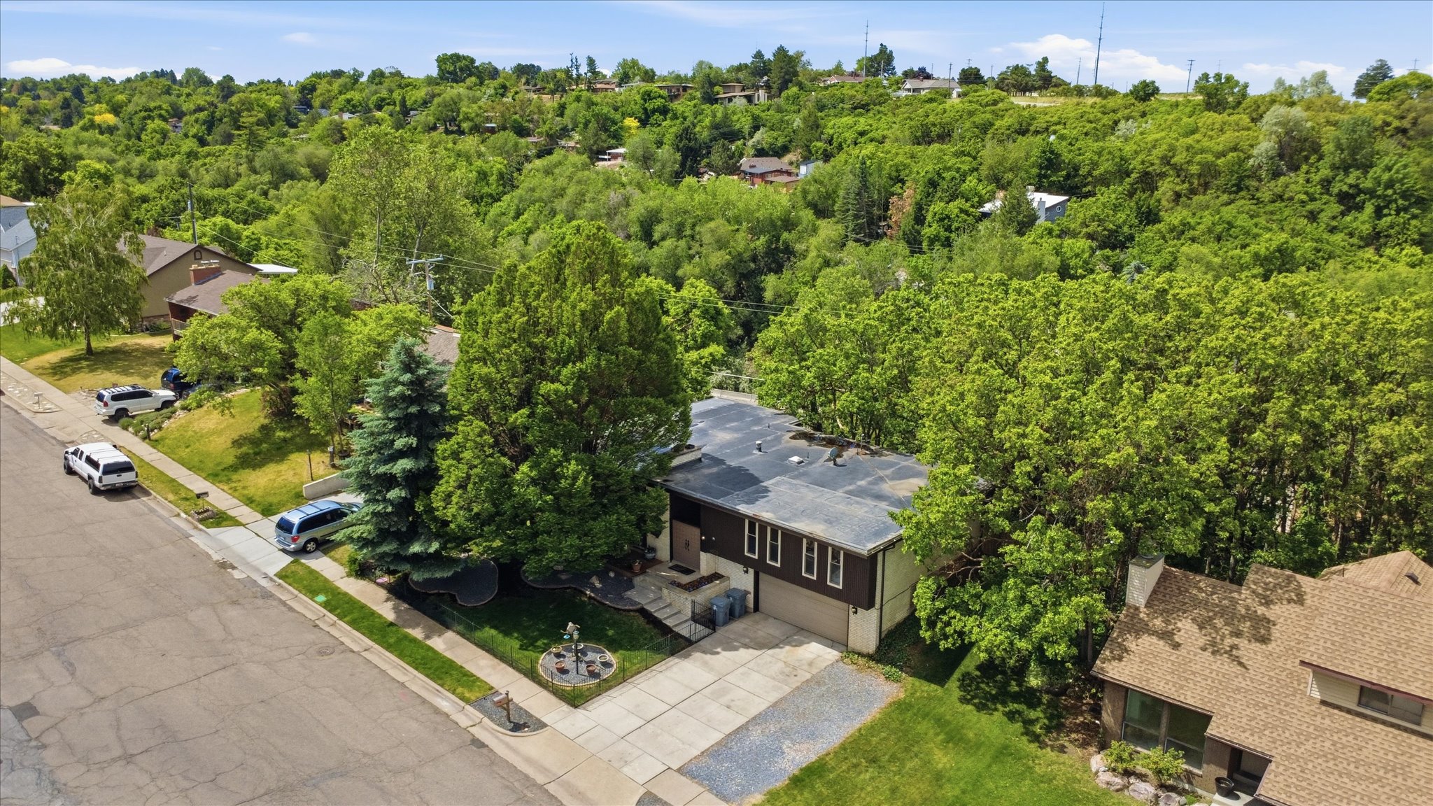Property exterior featuring a two-car garage, mature landscaping, and a sloped, tree-covered hillside backdrop
