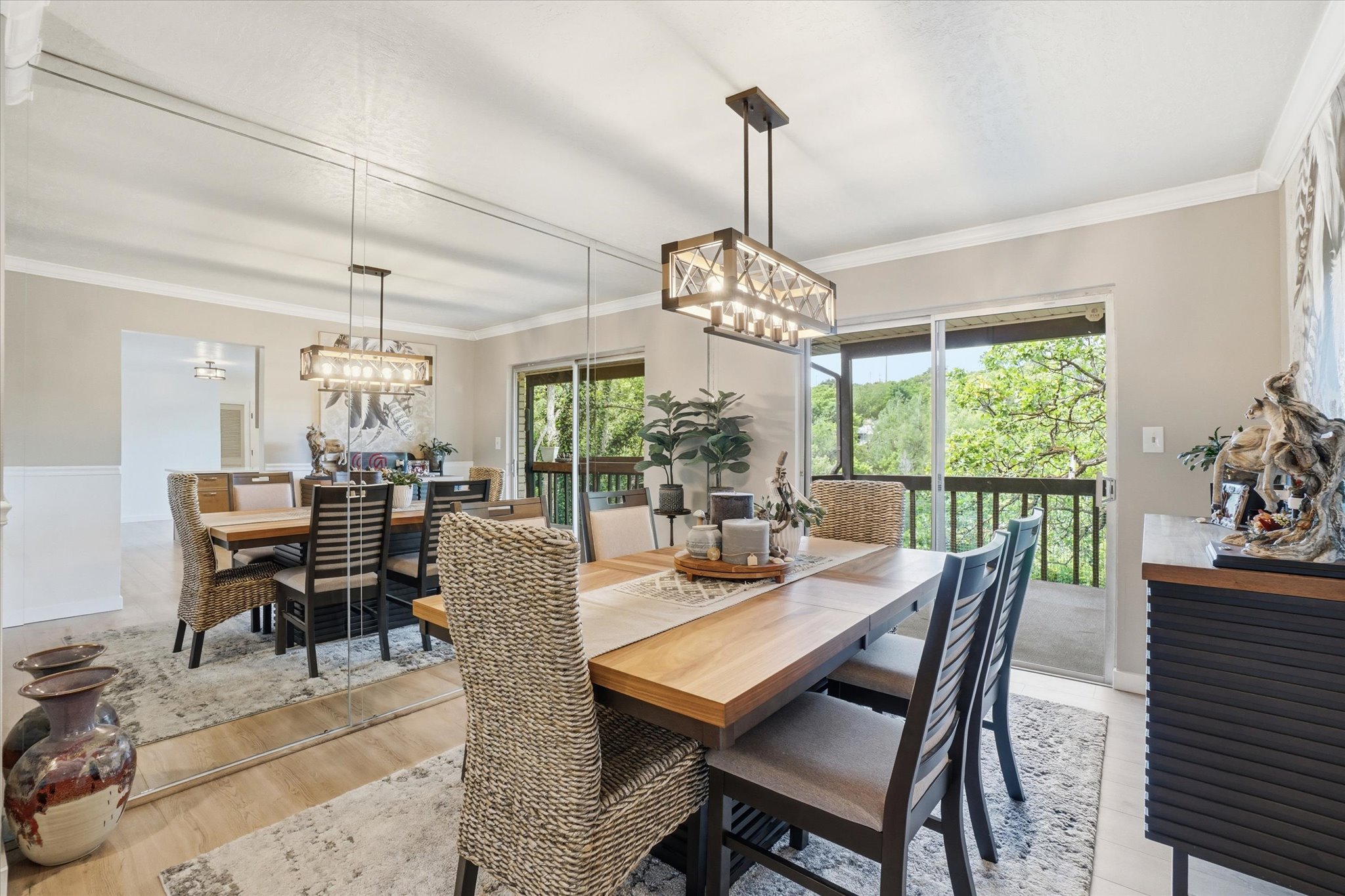 Dining area featuring wood-finish flooring, a contemporary linear chandelier, full-height mirrored wall, and a sliding glass door opening to an exterior balcony