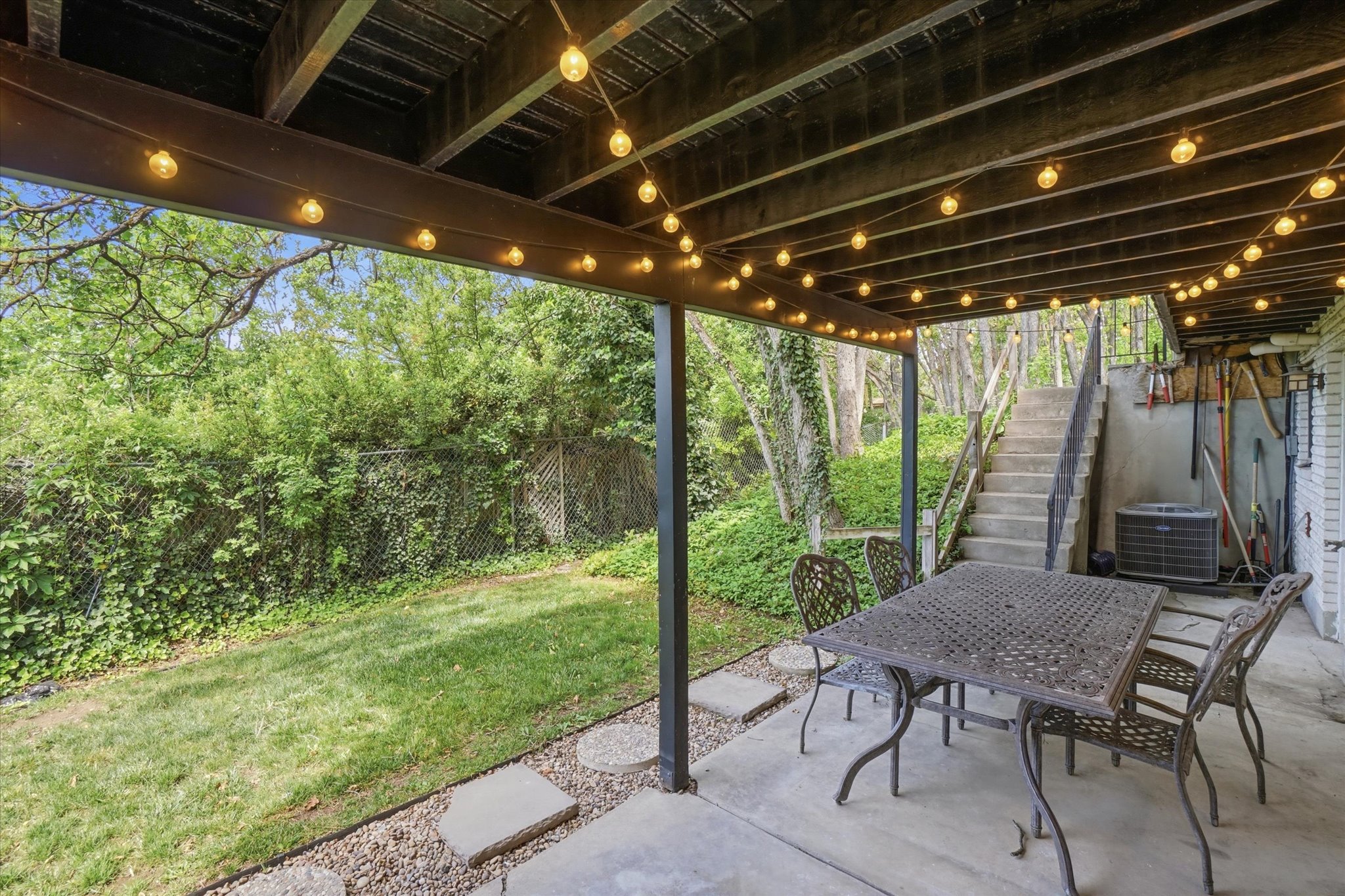 Covered concrete patio with overhead lighting, leading to a lawn area with mature perimeter foliage