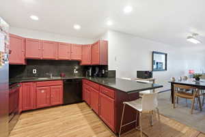 Kitchen featuring red cabinetry, dark countertops, wood-finish flooring, recessed lighting, and a built-in dishwasher