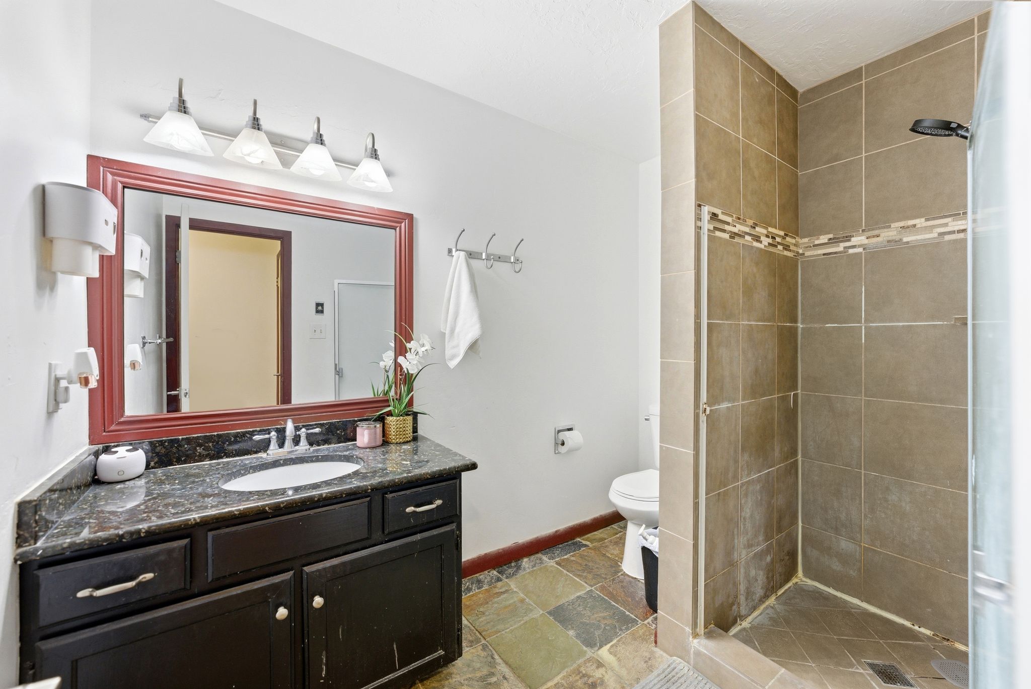 Bathroom featuring a dark wood vanity with a stone countertop, a framed mirror, and a walk-in shower with tile surround and decorative accent band
