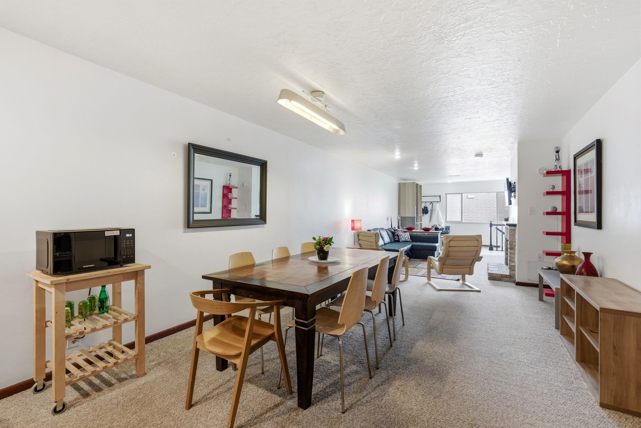 Open-concept living space featuring a dining area with a dark wood table, neutral carpeting, and white walls throughout