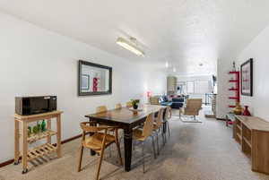 Open-concept living space featuring a dining area with a dark wood table, neutral carpeting, and white walls throughout