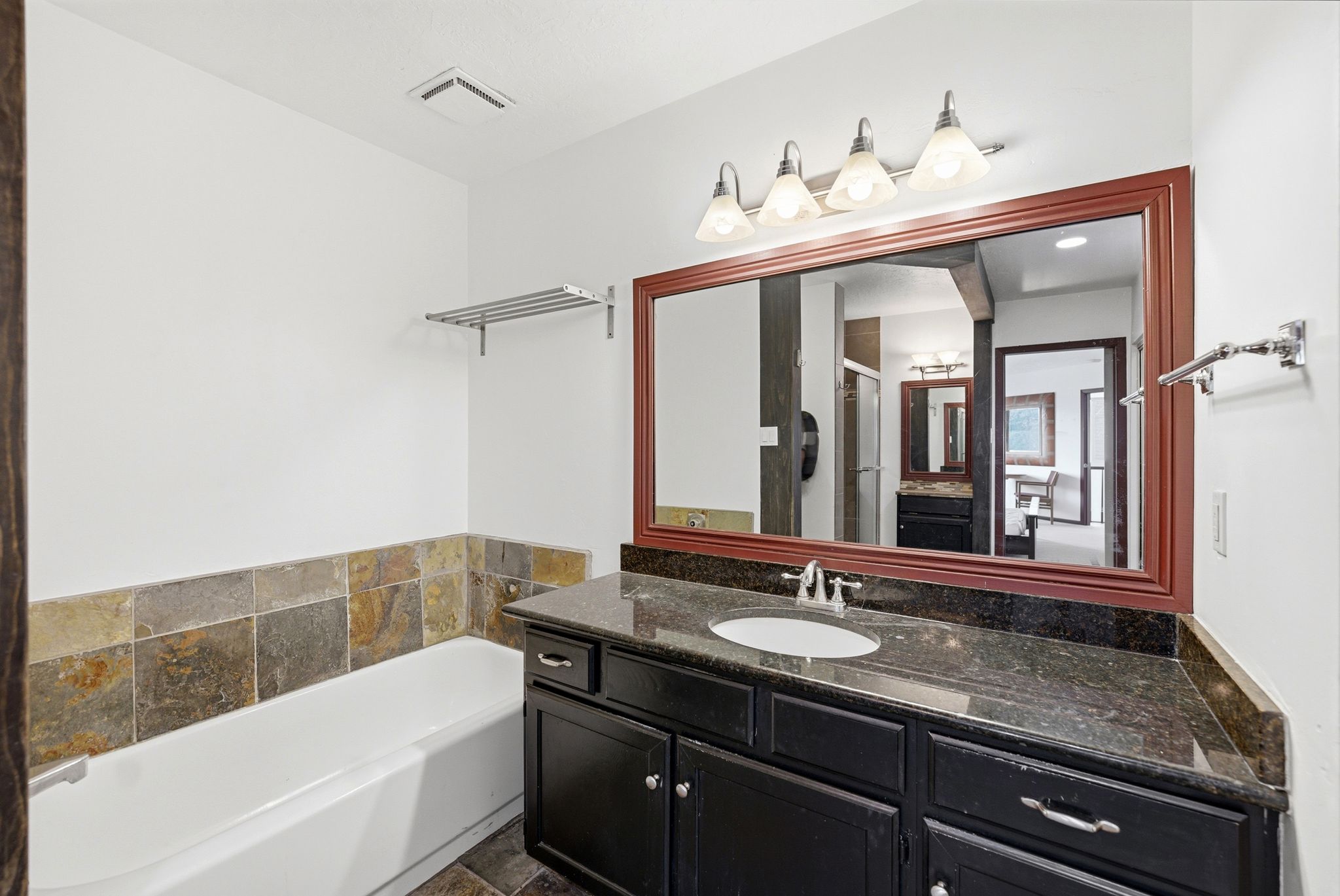 Bathroom featuring a dark wood-finish vanity with a single sink, dark countertop, and a large mirror with a wood-finish frame