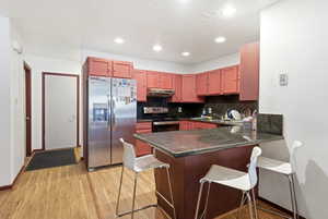 Kitchen featuring wood-finish flooring, recessed lighting, stainless steel appliances, dark stone countertops, and a peninsula with seating