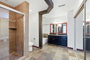 Spacious bathroom featuring a glass-enclosed shower with tile surround and integrated shelf, a vanity with dark cabinetry and countertop, a large framed mirror, and slate-finish floor tiles