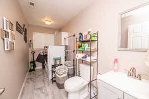Combined laundry and bathroom space featuring gray-toned flooring, a window with blinds, and white appliances