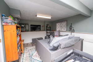 Finished lower-level space featuring wood-finish flooring, a painted beam ceiling, and wainscoting