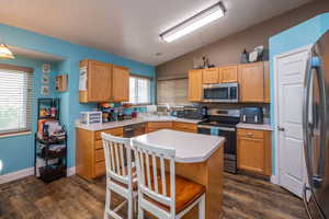 Kitchen featuring a central island, wood-finish flooring, light wood cabinetry, stainless steel appliances, and a vaulted ceiling