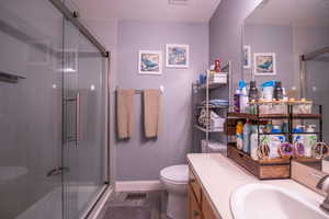 Bathroom featuring a glass-enclosed shower, wood-finish vanity with an integrated sink, broad wall mirror, and grey-toned flooring