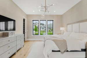 Spacious bedroom featuring light wood-finish flooring, a contemporary chandelier, a large upholstered headboard, and a three-panel window with black frames