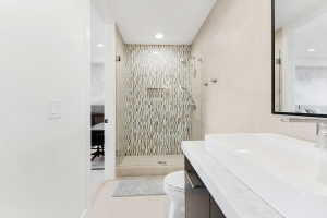 Contemporary bathroom featuring a glass-enclosed shower with mosaic tile, a sleek rectangular vessel sink, and a floating vanity with a light-colored countertop