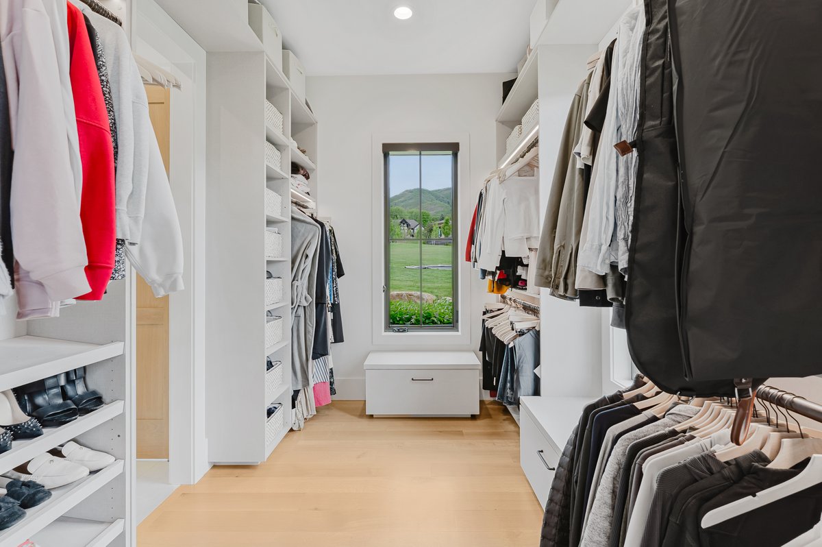 Custom closet featuring extensive built-in shelving, hanging rods, and light wood-finish flooring