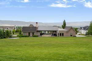 Expansive rear exterior featuring a stone and wood-paneled facade, a covered patio, a large green lawn, and distant mountains