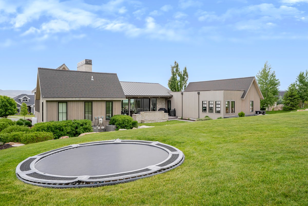 Expansive green lawn with a built-in trampoline, complemented by a contemporary exterior design featuring vertical siding and dark-trimmed windows