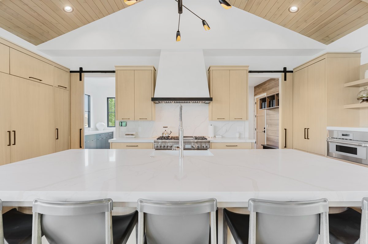 Spacious kitchen featuring a large white countertop island, integrated stainless steel appliances, and abundant light wood-finish cabinetry