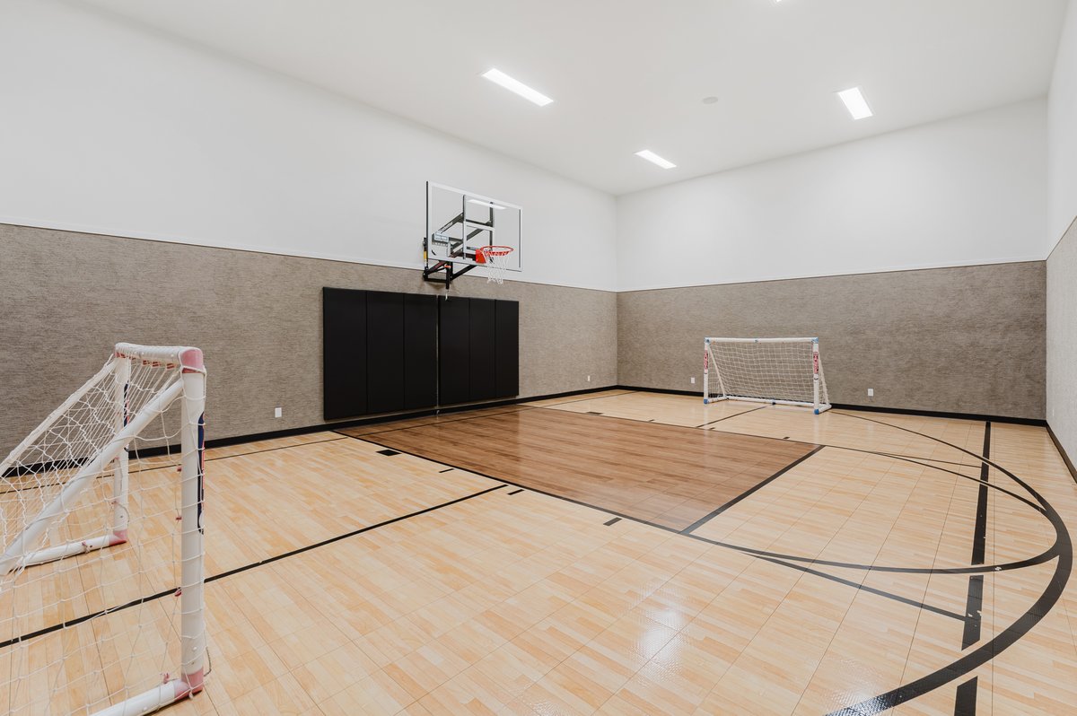 Indoor sport court featuring light wood-finish flooring with court markings, a basketball hoop, and padded wall sections