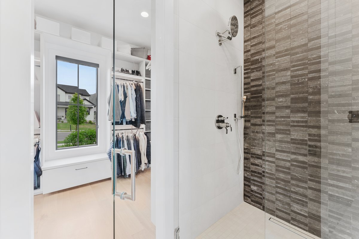 Spacious walk-in closet with custom built-in shelving, wood-finish flooring, and natural light from a large window
