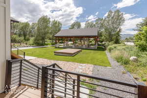 Outdoor gathering area featuring a covered pavilion with stone pillars, a wooden stage, and a manicured lawn
