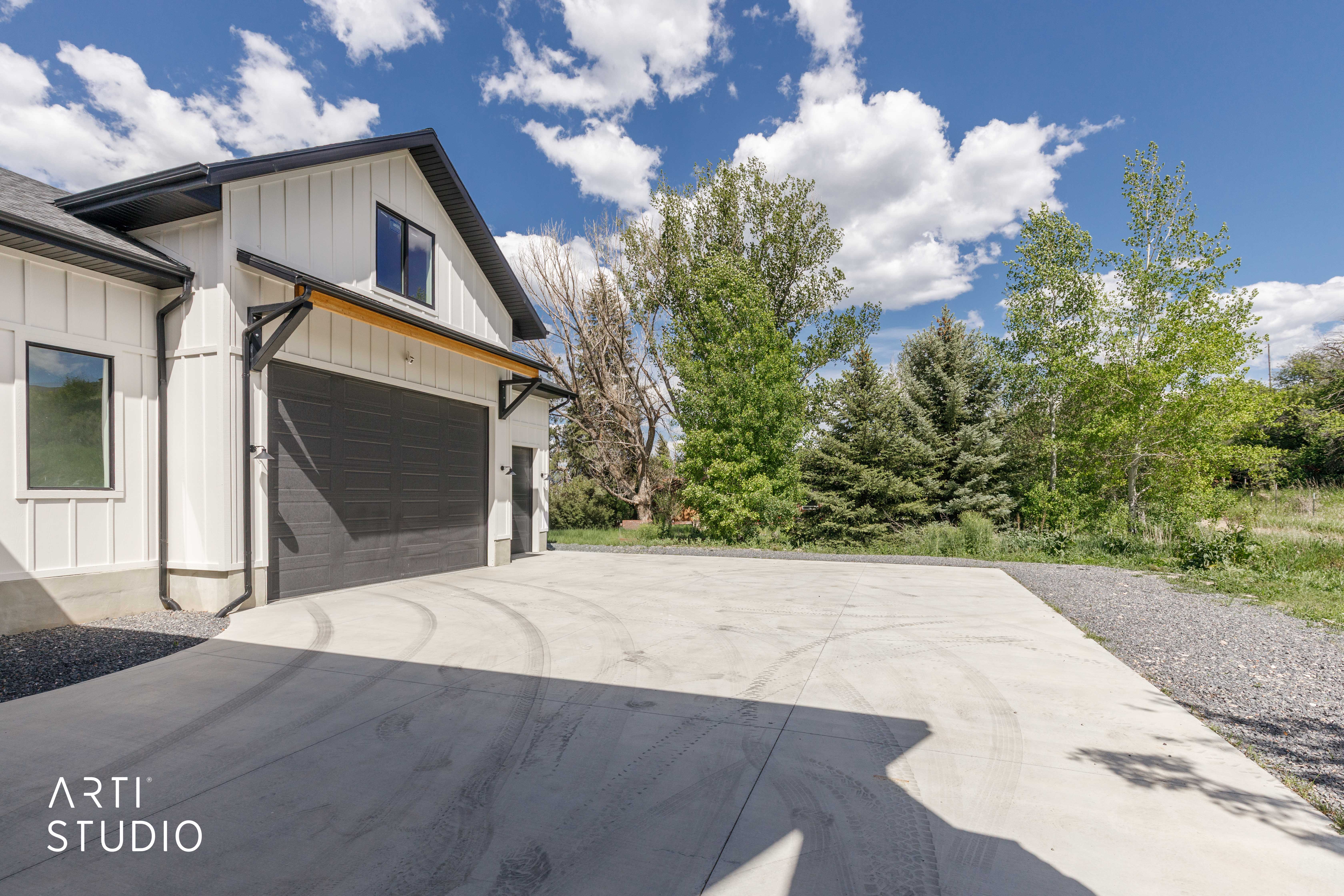 Modern farmhouse exterior featuring vertical white siding, a dark gray garage door, black-framed windows, and a concrete driveway