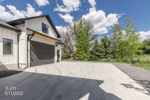 Modern farmhouse exterior featuring vertical white siding, a dark gray garage door, black-framed windows, and a concrete driveway