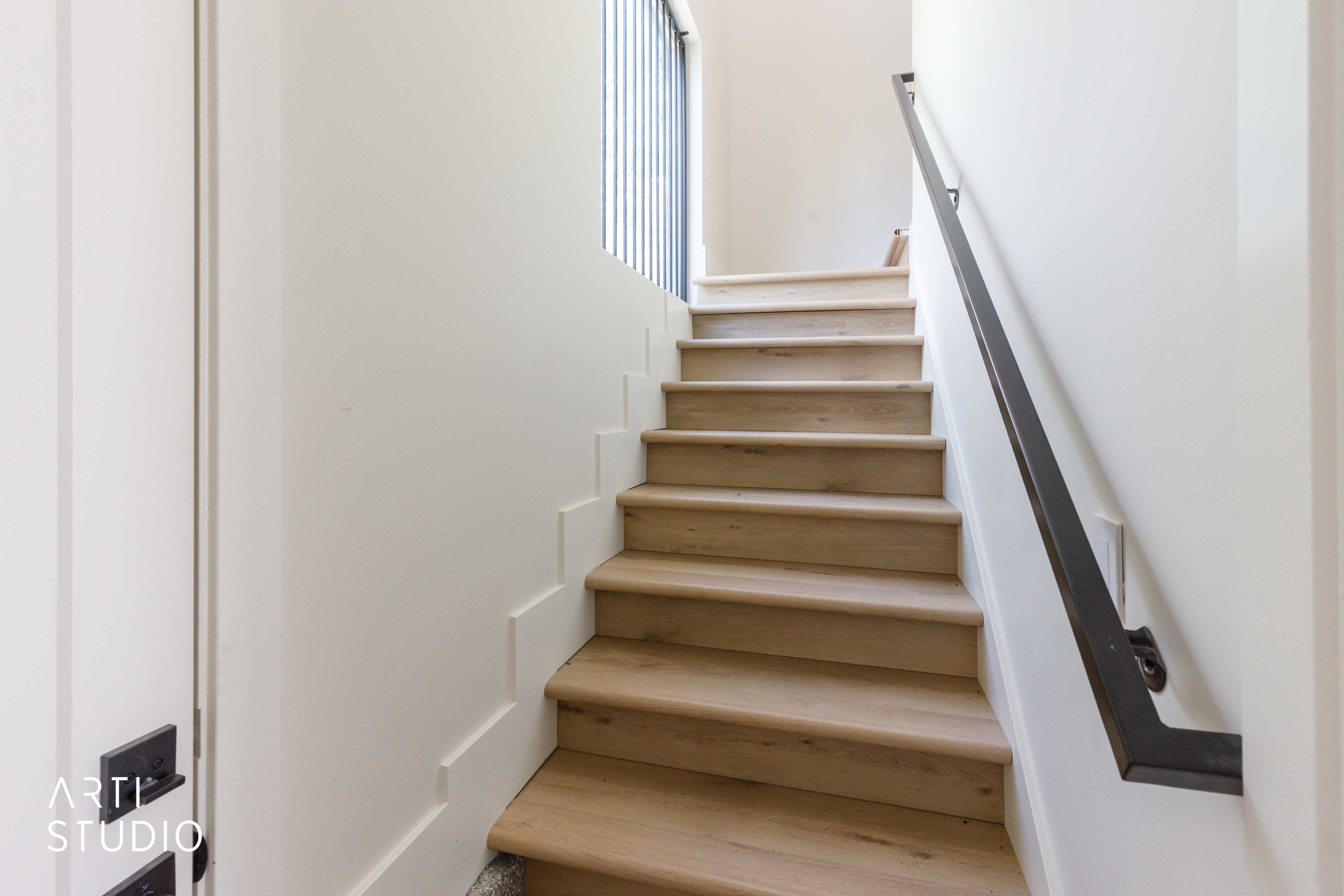 Staircase featuring wood-finish treads, white risers, a matte black handrail, and vertical balusters