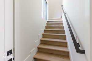 Staircase featuring wood-finish treads, white risers, a matte black handrail, and vertical balusters