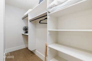 Walk-in closet featuring built-in white shelving, integrated hanging rods, and wood-finish flooring