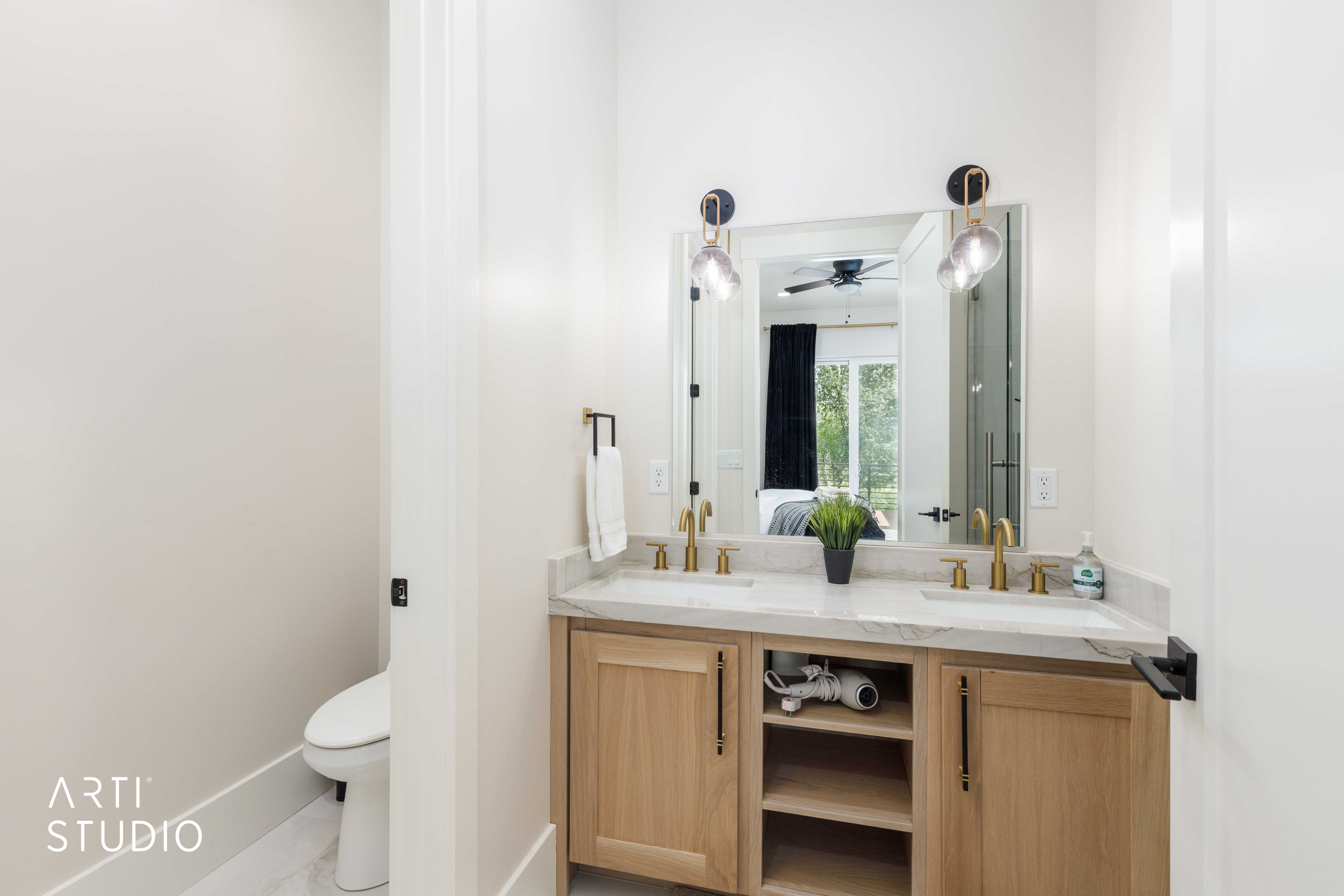 Dual vanity with wood-finish cabinetry, light-toned countertop, and gold-finish fixtures