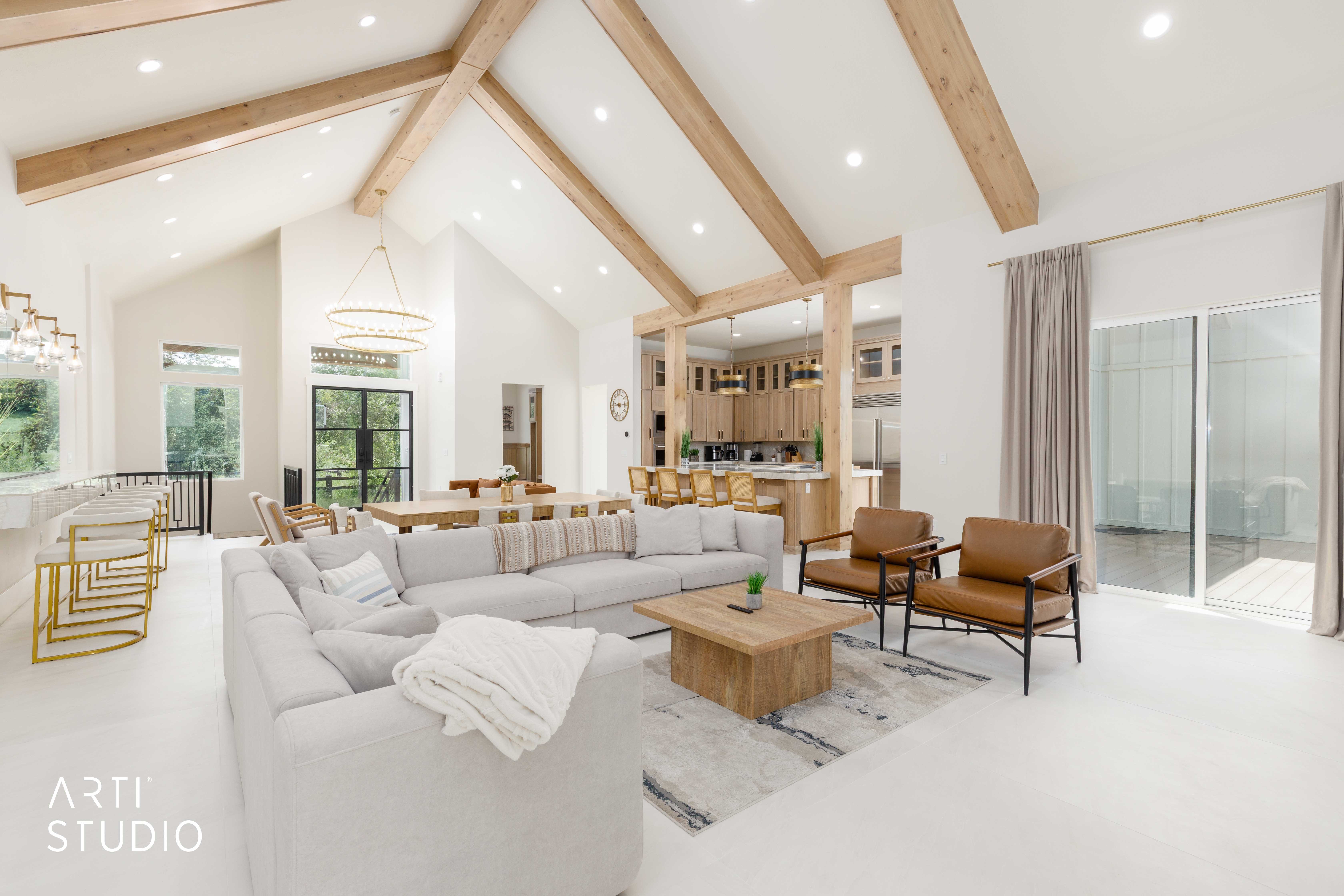Spacious open-concept living area featuring vaulted ceilings with exposed wood beams, recessed lighting, and expansive glass sliding doors