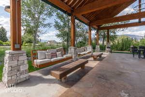 Expansive outdoor covered patio featuring exposed timber beams, stone-clad pillars, and a concrete floor