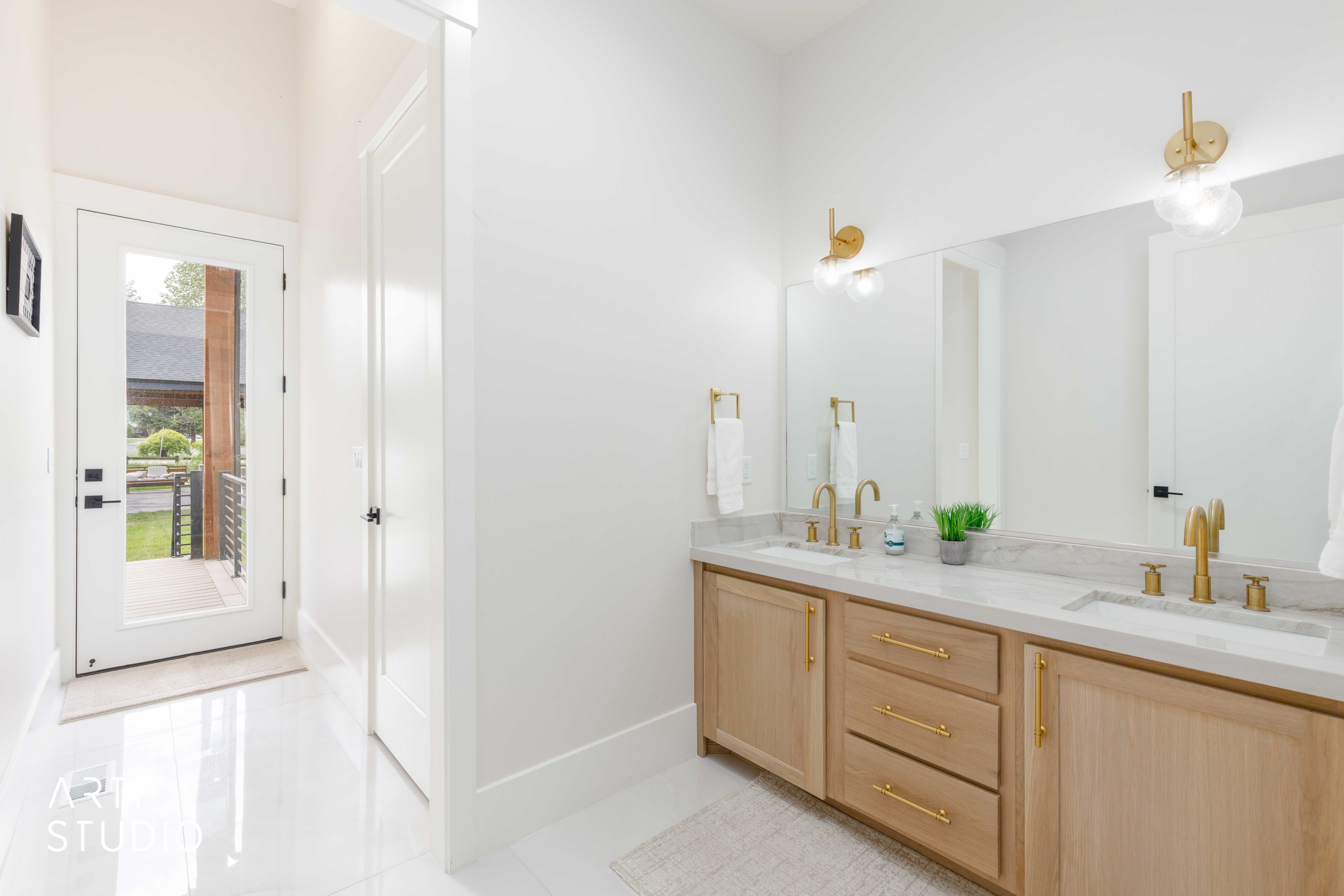 Double vanity with light wood-finish cabinetry, white countertop, and gold-finish fixtures