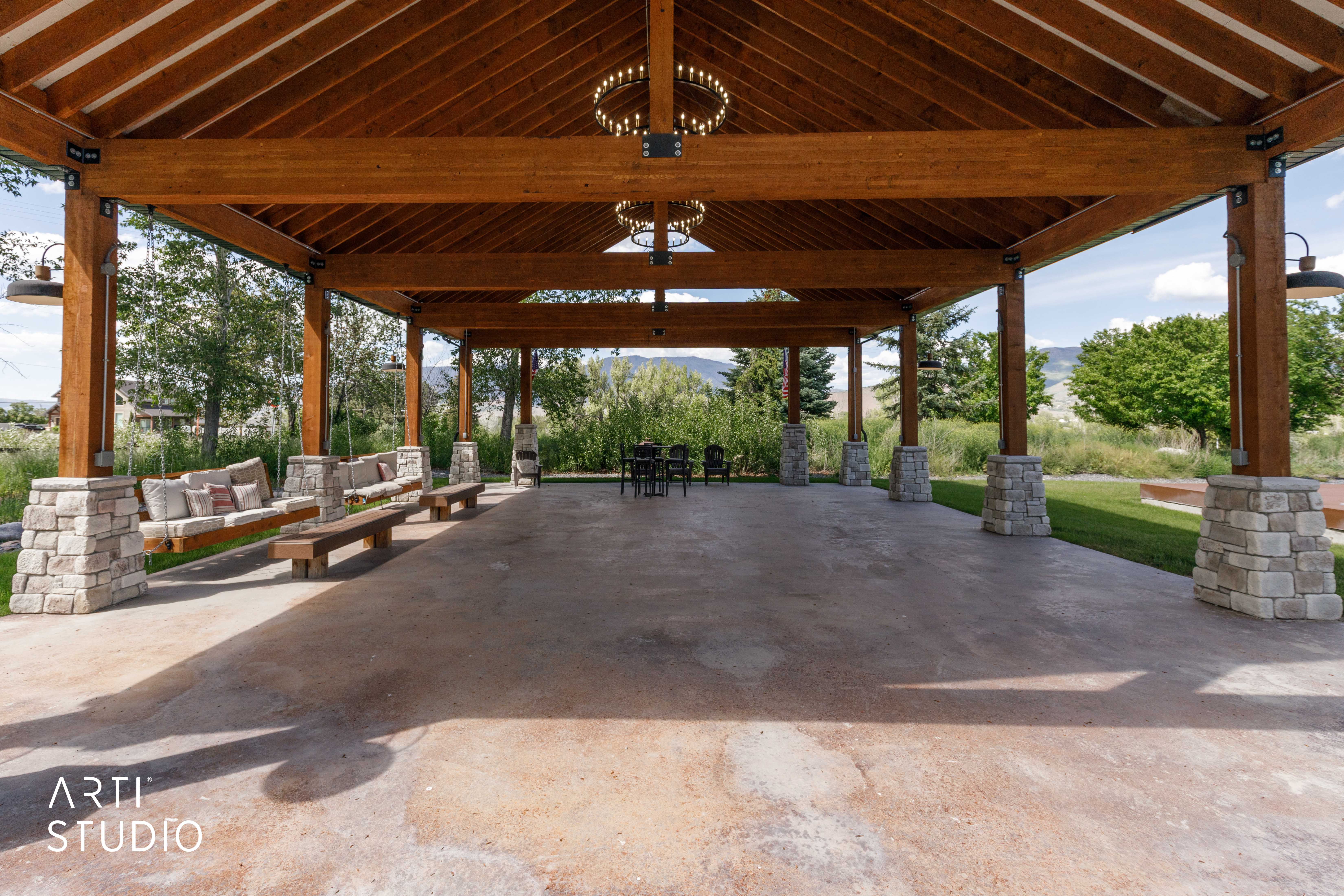 Expansive covered patio featuring a wood-beam ceiling, stone-wrapped columns, concrete flooring, and built-in swing seating